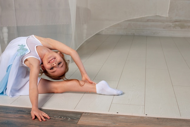 Chica guapa hace gimnasia con un vestido en el fondo de una cortina blanca