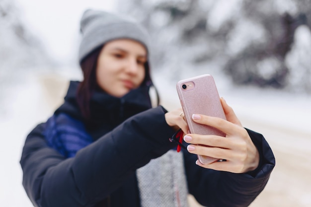 Una chica guapa hace un selfie en medio de un camino forestal nevado.