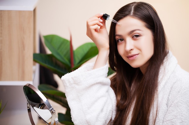 Chica guapa haciendo procedimientos cosméticos en casa frente al espejo.