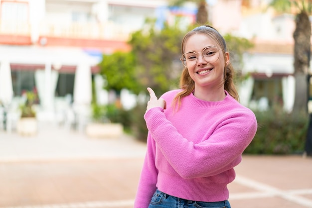 Chica guapa joven al aire libre con gafas y apuntando hacia el lado