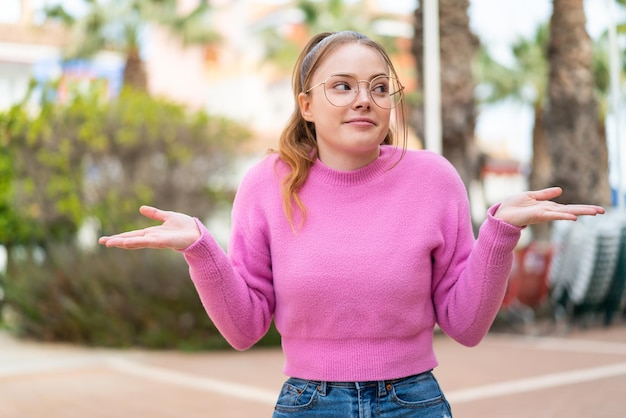 Foto chica guapa joven al aire libre con gafas y dudas