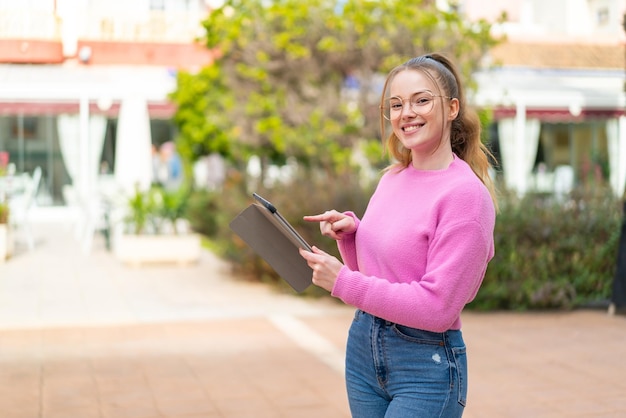 Chica guapa joven al aire libre tocando la pantalla de la tableta con expresión feliz