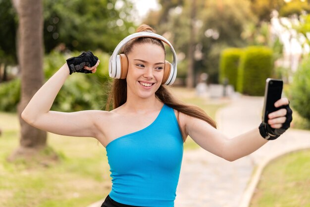 Chica guapa joven al aire libre usando ropa deportiva y tomando una selfie con el móvil