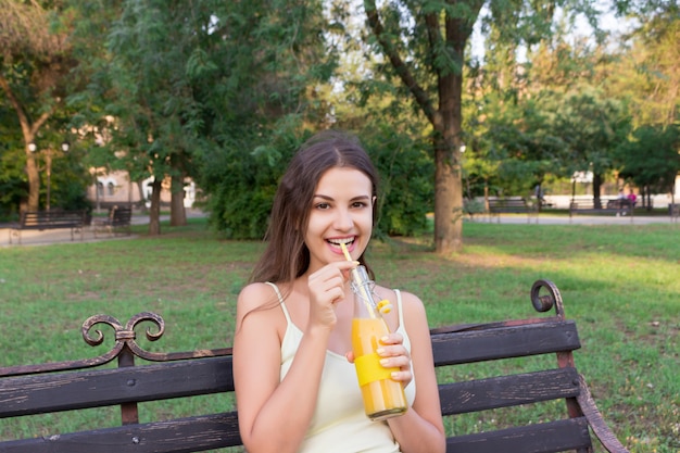 Chica guapa joven bebiendo limonada en el parque