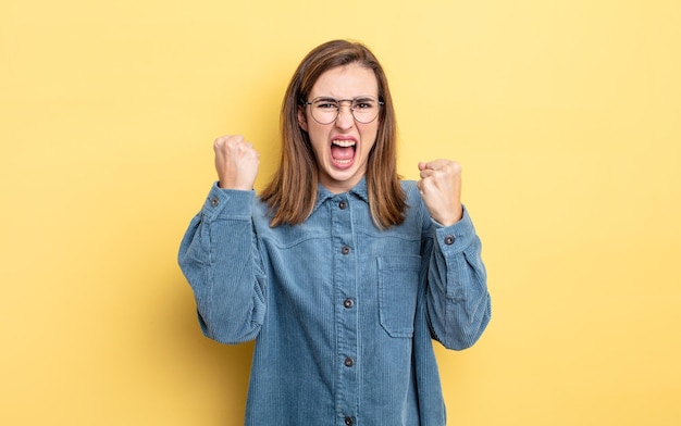 Chica guapa joven gritando agresivamente con una expresión de enojo o con los puños cerrados celebrando el éxito