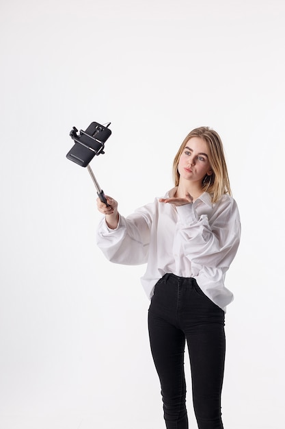 Chica guapa joven haciendo autorretrato con teléfono inteligente conectado a selfie stick