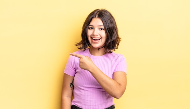 Chica guapa joven que parece emocionada y sorprendida apuntando hacia un lado y hacia arriba para copiar el espacio