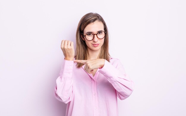 Chica guapa joven que parece impaciente y enojada, apuntando al reloj, pidiendo puntualidad, quiere llegar a tiempo