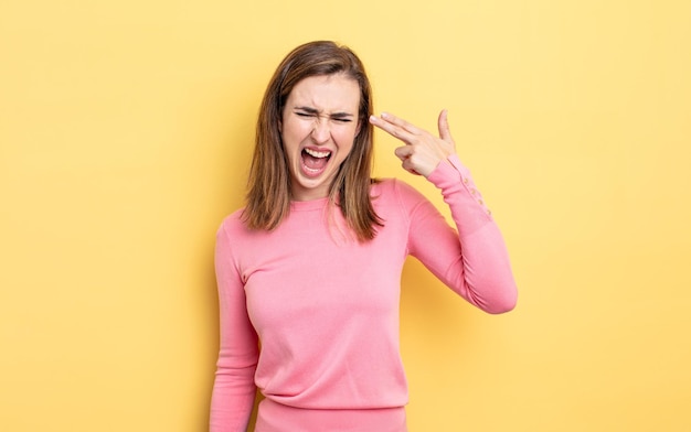 Chica guapa joven que parece infeliz y estresada, gesto de suicidio haciendo un signo de pistola con la mano, apuntando a la cabeza