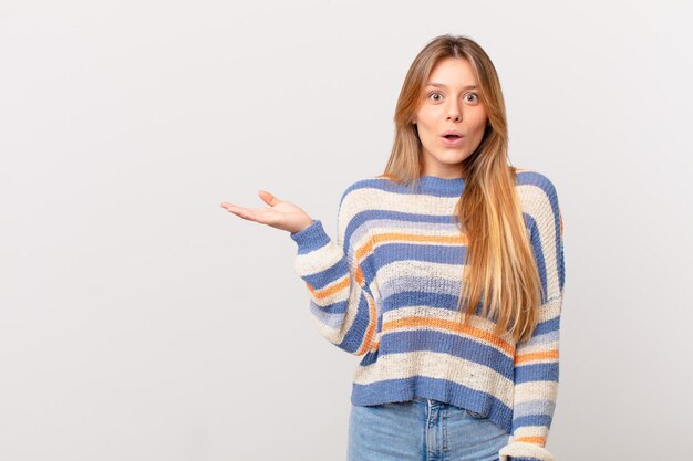 Chica guapa joven que parece sorprendida y conmocionada, con la mandíbula caída sosteniendo un objeto