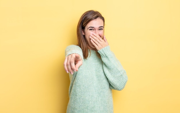 Chica guapa joven que se ríe de ti, apunta a la cámara y se burla o se burla de ti