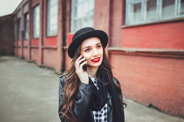 Chica guapa joven con sombrero usando el teléfono. Mujer usando el teléfono para hacer una llamada en la calle