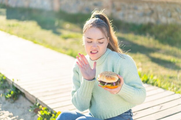 Chica guapa joven sosteniendo una hamburguesa al aire libre