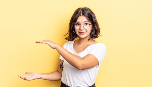 Chica guapa joven sosteniendo un objeto con ambas manos en el espacio de copia lateral, mostrando, ofreciendo o publicitando un objeto