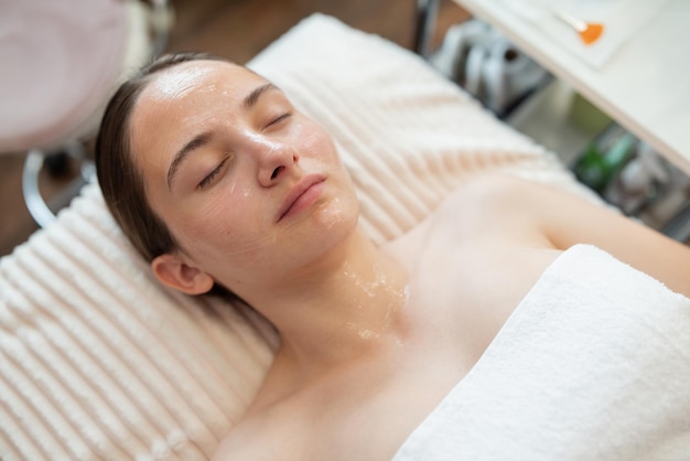 Chica guapa joven tumbada en el sofá con los ojos cerrados gel líquido en la cara para el procedimiento ultrasónico Cosmetología cuidado de la piel hidratando y suavizando los conceptos de la piel