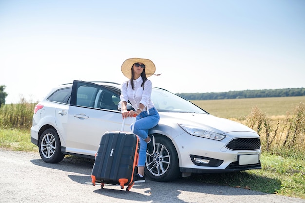 Chica guapa con maleta de pie cerca del coche y wiat para su viaje de ensueño