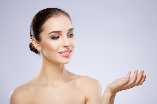 Chica guapa con maquillaje desnudo posando en el fondo gris del estudio, concepto de fotografía de belleza, piel perfecta, producto de sujeción.