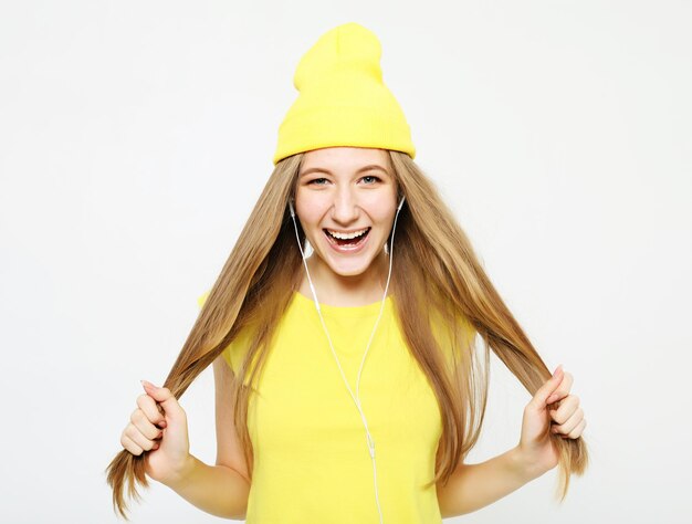 Chica guapa de moda con auriculares escuchando música con sombrero amarillo y camiseta