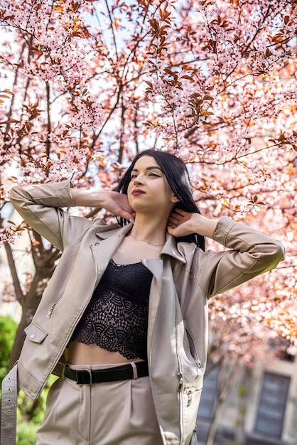 Chica guapa de moda posando cerca de ramas de árboles florecientes en primavera