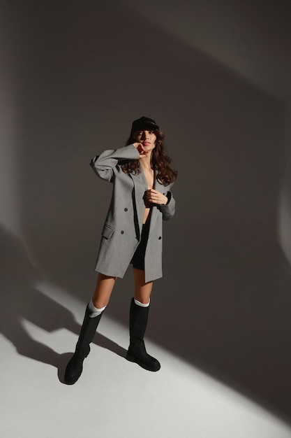 Chica guapa modelo en un sujetador blazer de gran tamaño de moda y botas de moda sobre fondo gris