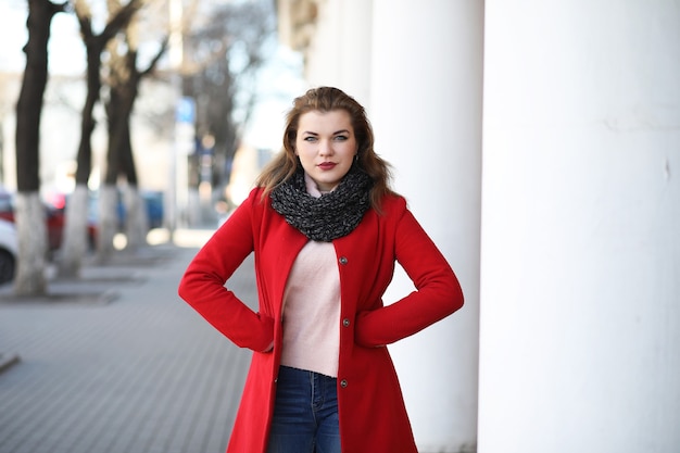 Chica guapa en un paseo en abrigo rojo en la ciudad