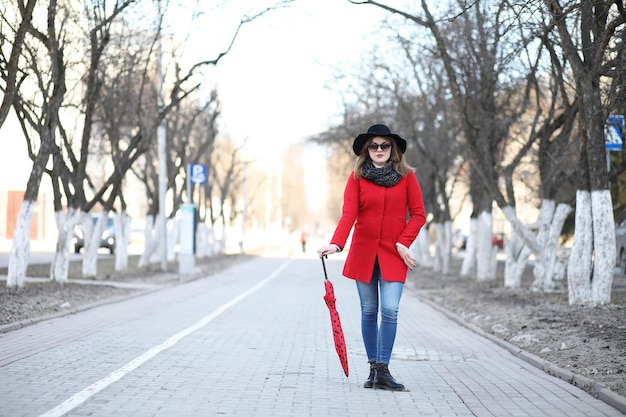 Chica guapa en un paseo con sombrilla roja en la ciudad