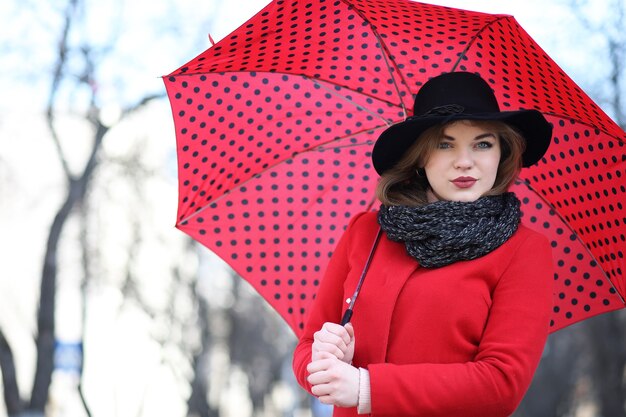 Chica guapa en un paseo con sombrilla roja en la ciudad