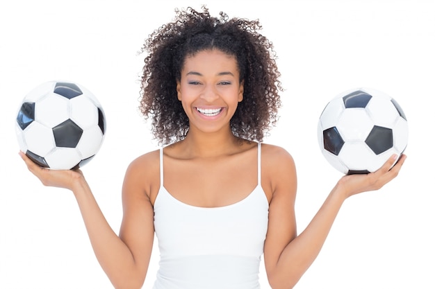 Chica guapa con peinado afro sonriendo a la cámara con balones de fútbol