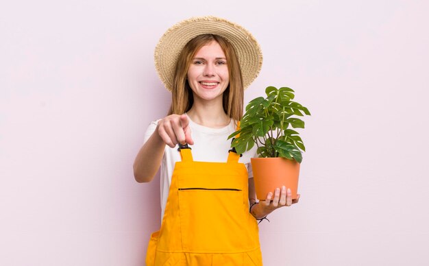 Chica guapa pelirroja apuntando a la cámara eligiendo tu planta y concepto de jardinería