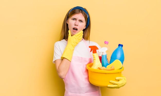 Chica guapa pelirroja con la boca y los ojos bien abiertos y la mano en el mentón concepto de ama de llaves