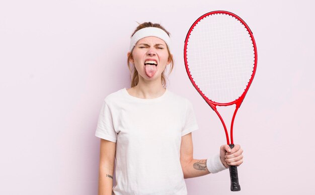 Chica guapa pelirroja sintiéndose disgustada e irritada y sacando la lengua concepto de tenis