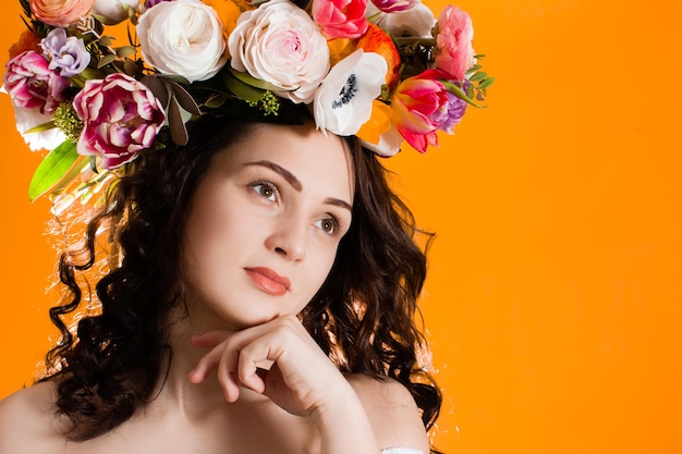 La chica guapa con el pelo rizado y corona de flores en la cabeza, primer plano sobre fondo naranja