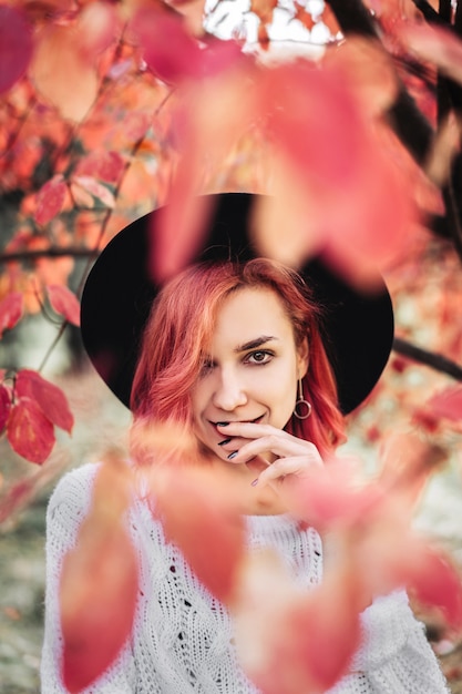 Chica guapa con el pelo rojo y sombrero caminando en el parque, tiempo de otoño.