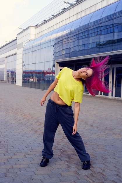 Una chica guapa con el pelo teñido de rosa y una camiseta amarilla en ropa deportiva agita su cabello