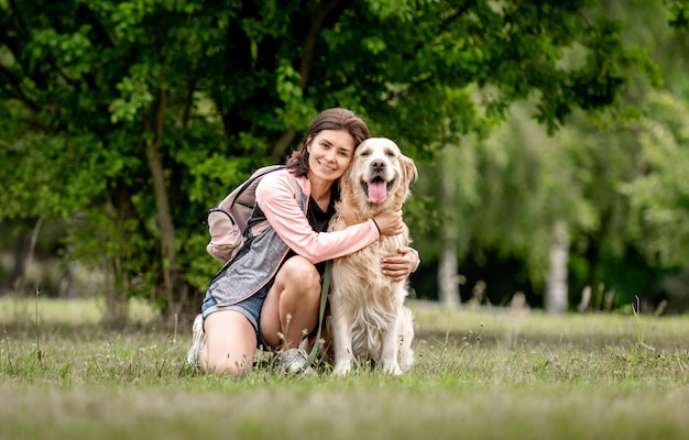 Chica guapa con perro golden retriever sentado en la naturaleza hermosa mujer joven abrazando mascota de pura raza