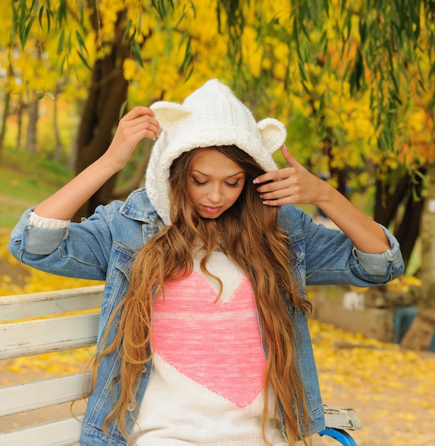 Chica guapa con un sombrero de oso de punto posando en el parque de otoño.