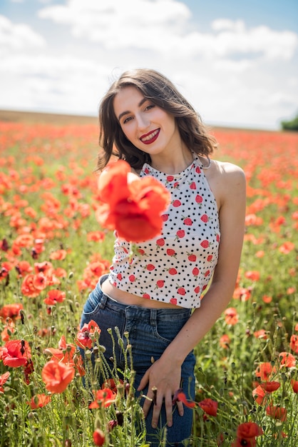 Chica guapa soñando y disfrutando de la naturaleza en el campo de amapolas rojas. Hora de verano