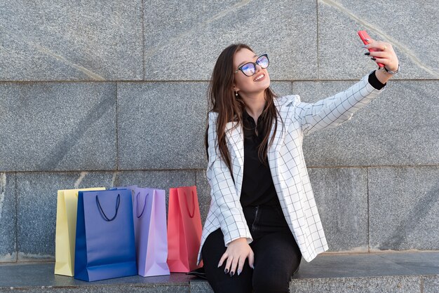 Chica guapa sosteniendo bolsas con smartphone y sonriendo