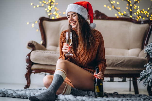 Chica guapa en suéter y sombrero de Navidad bebiendo champán