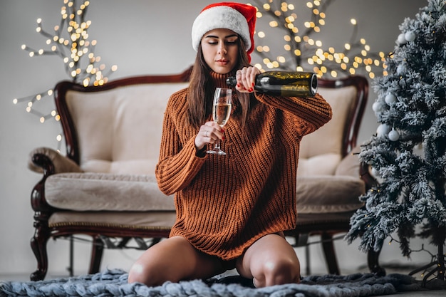 Chica guapa en suéter y sombrero de Navidad bebiendo champán