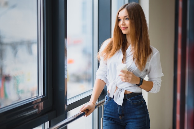 Chica guapa tomando café junto a la ventana