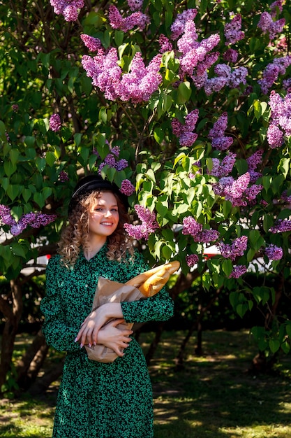 Chica guapa vestida a la francesa con baguette en mano y en lila. París de estilo francés. Mujer francesa de primer plano en ropa elegante sosteniendo baguettes frescas y sonriendo. Lugar para inscripción o logo.