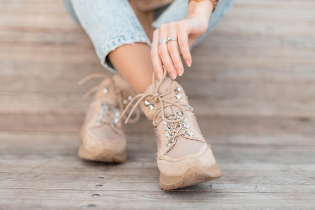 Chica guapa con zapatos de cuero de moda ata sus cordones y se sienta en un piso de madera