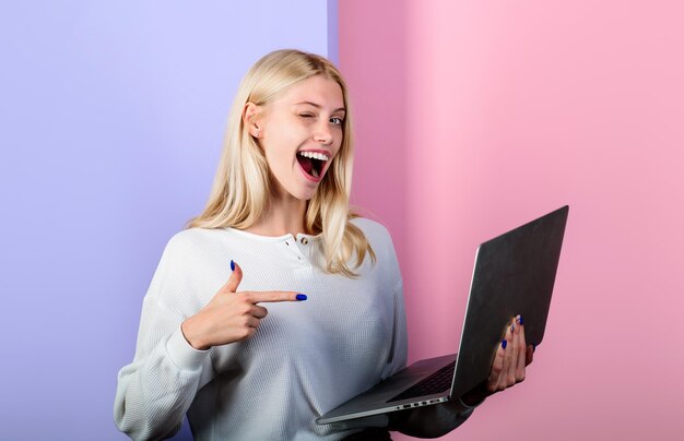 Chica guiñando el dedo hacia la computadora portátil modelo femenino sosteniendo la computadora presentando publicidad nueva