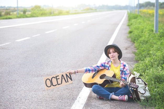 Chica con guitarra haciendo autostop