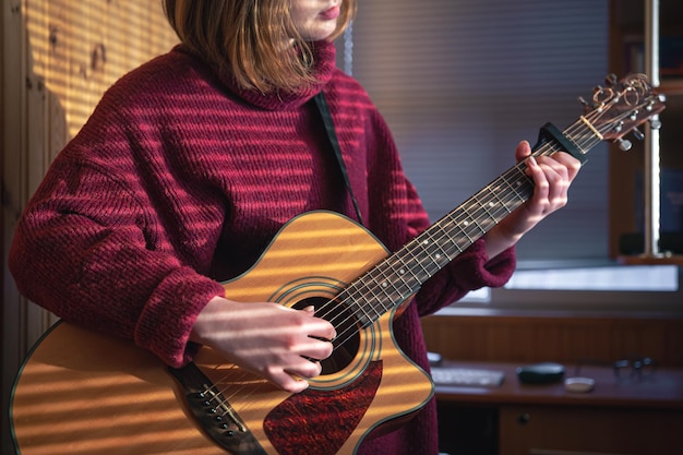 Chica con una guitarra en la luz del sol a través de las persianas.