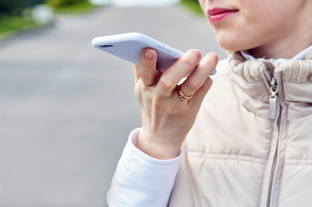 Chica habla un mensaje de voz en un teléfono inteligente en el verano en la calle.