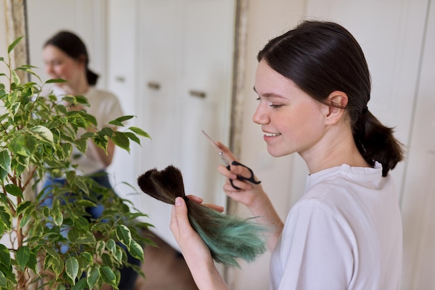 Foto chica hace un corte de pelo en casa, adolescente se corta el pelo, en manos montón de pelo cortado y tijeras, corte de pelo teñido no saludable