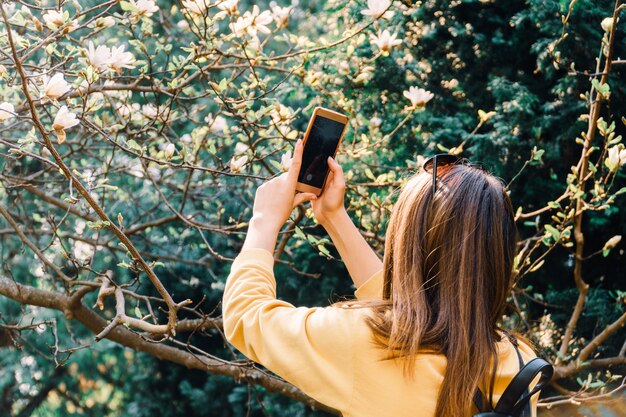 Chica hace foto de flor de magniloa en la cámara del teléfono inteligente. medios de comunicación social