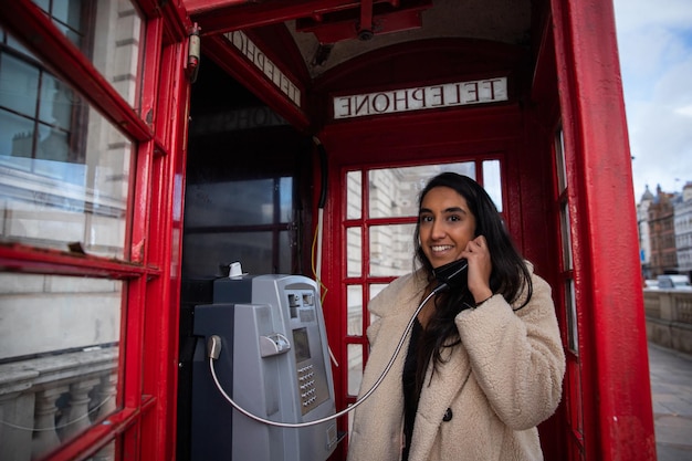 Foto chica hace una llamada telefónica dentro de una cabina telefónica roja en londres. hermosa mujer sonriente y atractiva por teléfono